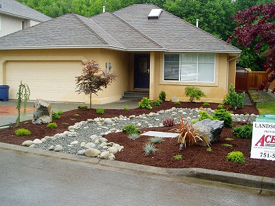 Landscaped front yard of a residential home featuring a dry river bed and fresh shrub plantings in bark mulch