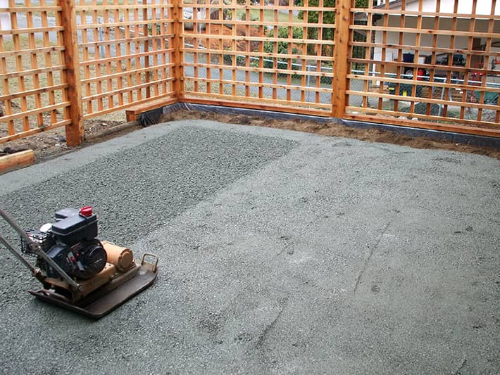 A gas-powered plate compactor tamps sand and gravel in preparation for a paver patio installation in Nanaimo, BC